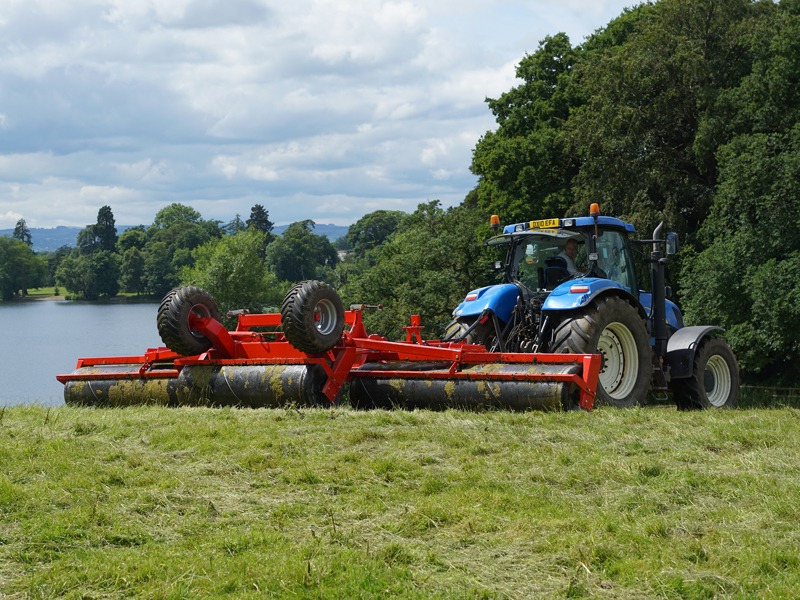 8.2m HE-VA hydraulic-folding Grass Rolls behind a New Holland tractor with lake background